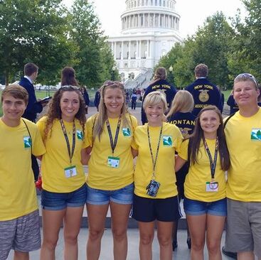 Six high school students in yellow shirts smiling in front of the U.S. White House.